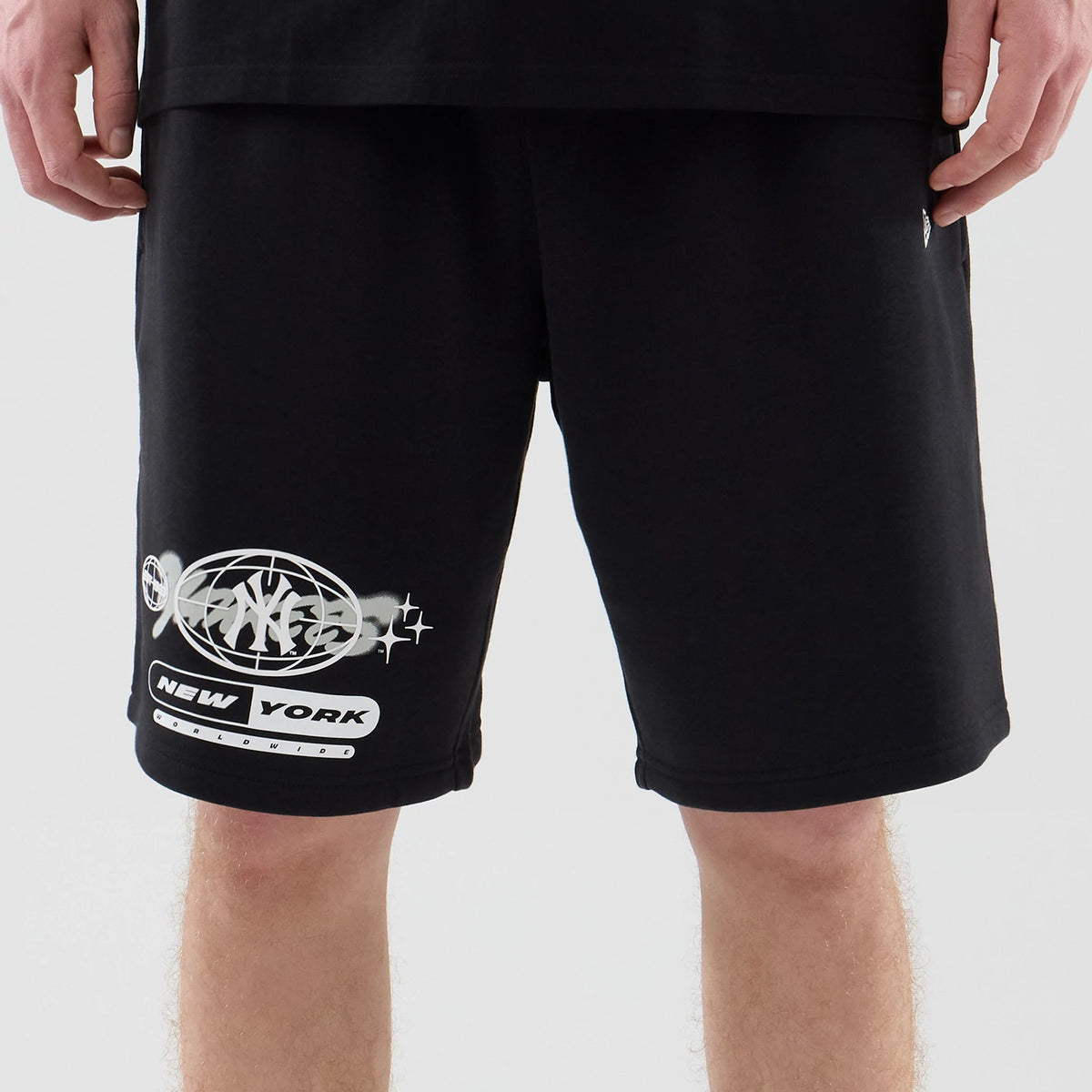 New Era New York Yankees MLB Logo Graphic Black Oversized Shorts, front view showing white graffiti-inspired graphics featuring the Yankees logo and the words New York on the left leg, on-model with casual styling.