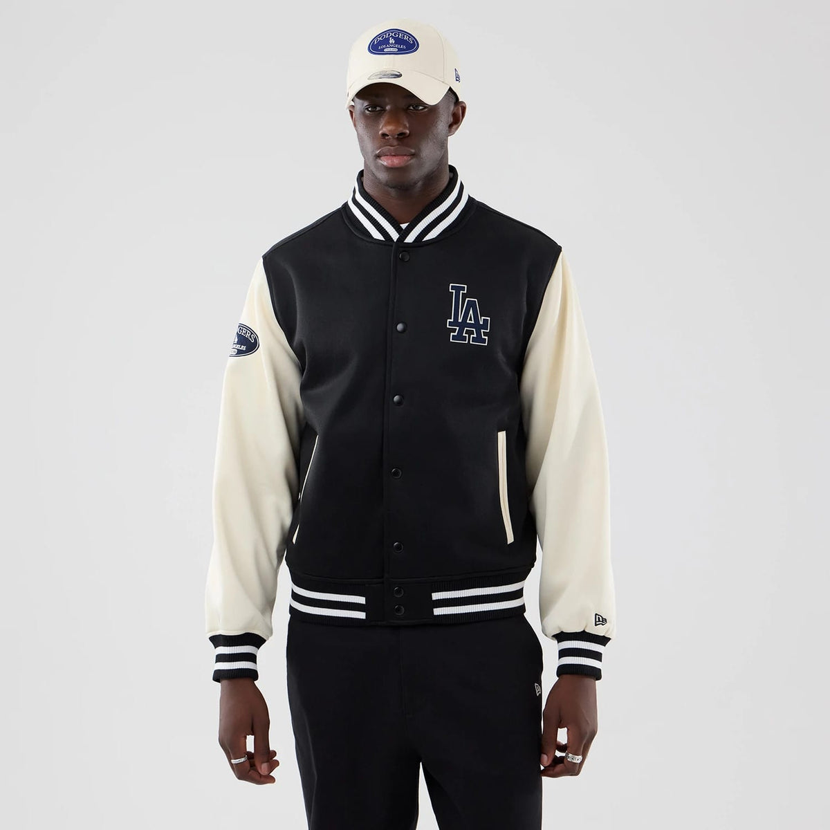 New Era LA Dodgers MLB Jersey Bomber Black Jacket, front view on-model showing the black and cream sleeves with black embroidered LA logo on the left chest, team patch on the right sleeve, and striped black and white cuffs and waistband.