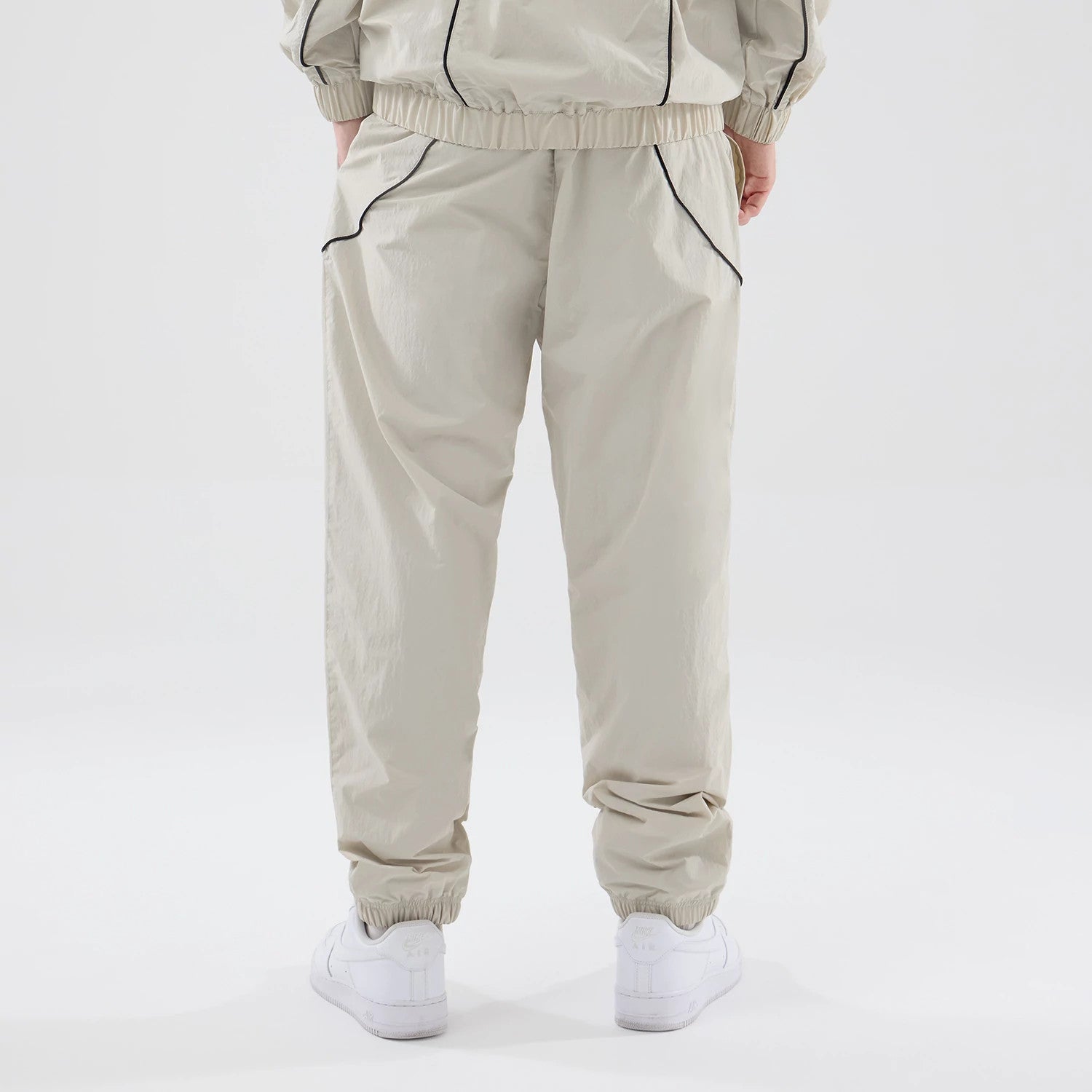 New Era New York Yankees MLB Piping Track Cream Track Pants, back view on a model with hands in pockets, showing black piping detail along the side seams, elasticated waistband and cuffs, and a relaxed fit over white trainers.