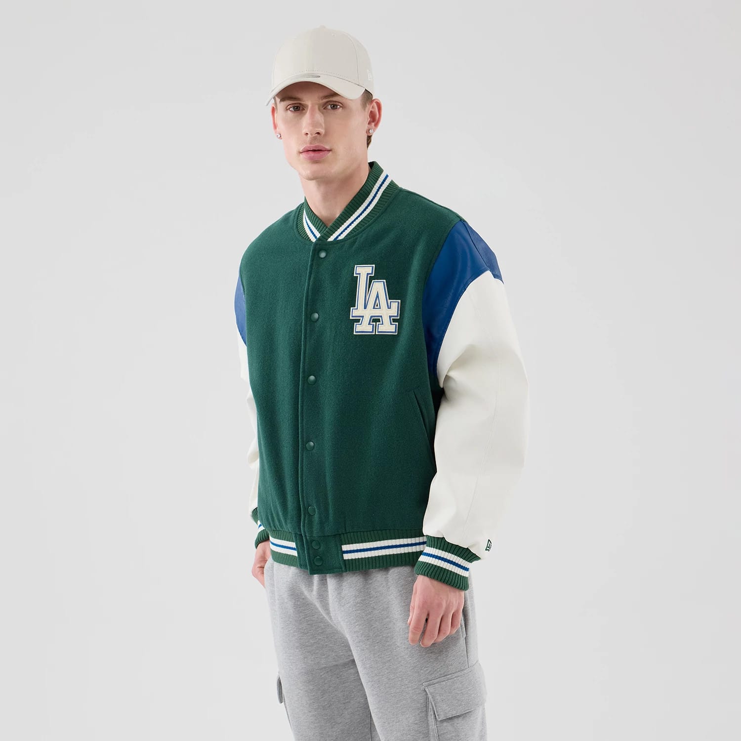 New Era LA Dodgers MLB Varsity Dark Green Jacket, front view on-model showing the white embroidered LA logo on the chest, dark green body with contrasting blue and white sleeves, and striped green and white ribbed collar, cuffs, and hem.
