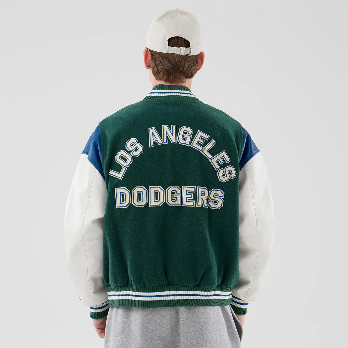 New Era LA Dodgers MLB Varsity Dark Green Jacket, back view on-model showing large embroidered Los Angeles Dodgers lettering in white with a blue outline across the shoulders, dark green body.