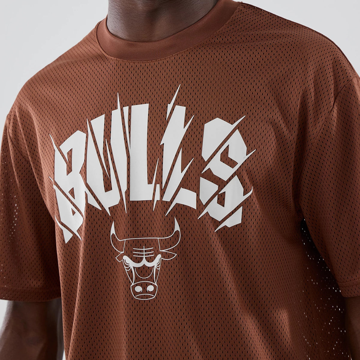 New Era Chicago Bulls NBA Core Plus Mesh Brown Oversized T-Shirt, front view on a model showing white printed BULLS lettering with sharp angles across the chest, complemented by the Chicago Bulls logo underneath and mesh texture throughout.