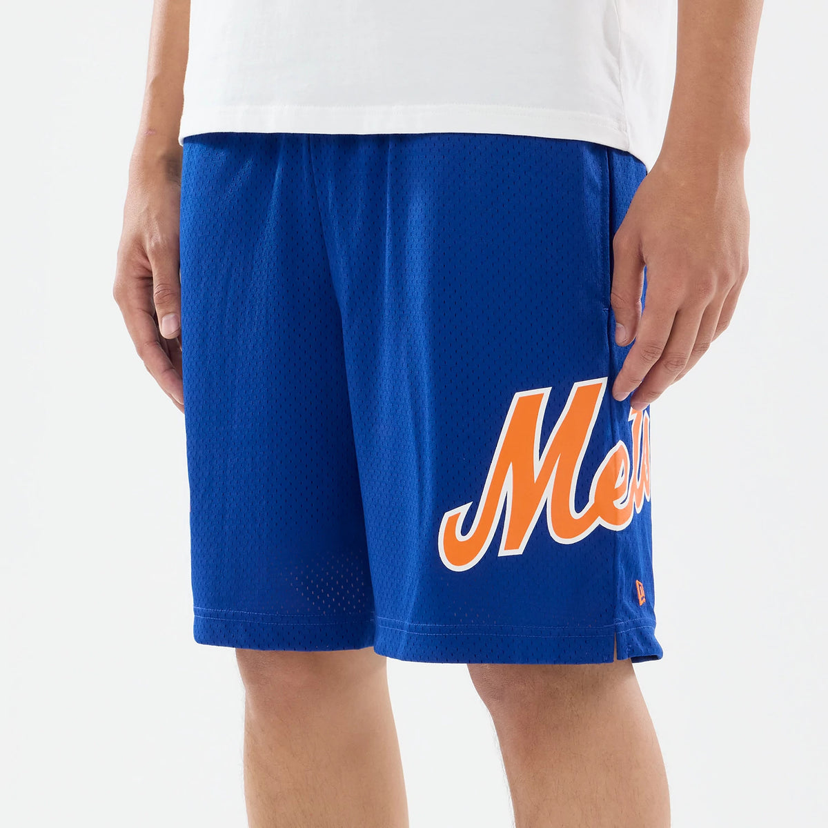 New Era New York Mets MLB Evergreen Blue Shorts, front view on-model featuring blue shorts with orange Mets script lettering on the left leg, small embroidered New Era logo near the hem, styled with a white shirt.