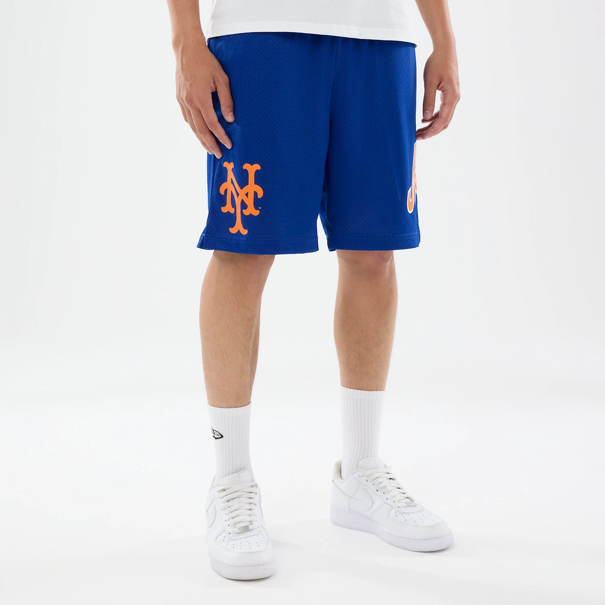 New Era New York Mets MLB Evergreen Blue Shorts, front view on a model showcasing the blue shorts with a large orange printed Mets logo on the left thigh, complemented by a smaller matching logo on the right, worn above white trainers.