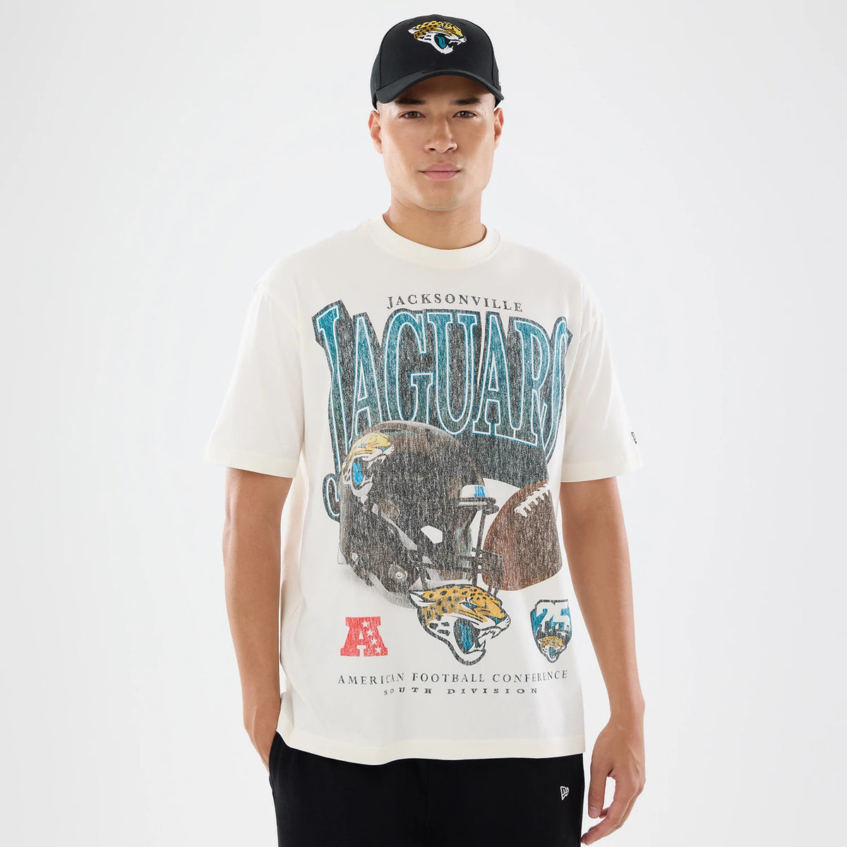 New Era Jacksonville Jaguars NFL Sport Classic Cream T-Shirt, front view on a model with a black cap, showing Jaguars lettering in blue, a large graphic of a helmet and football, and team logos including the Jaguars' emblem towards the bottom.