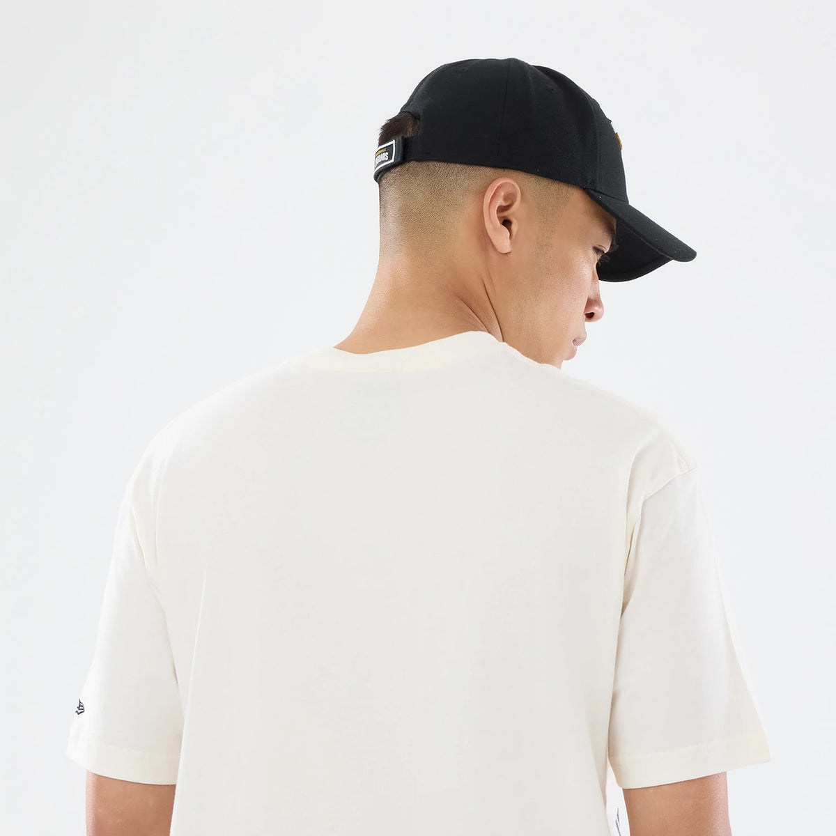 New Era Jacksonville Jaguars NFL Sport Classic Cream T-Shirt, back view on-model showcasing the plain cream back, a black cap with a rear tag, and the embroidered New Era logo on the left sleeve near the cuff.