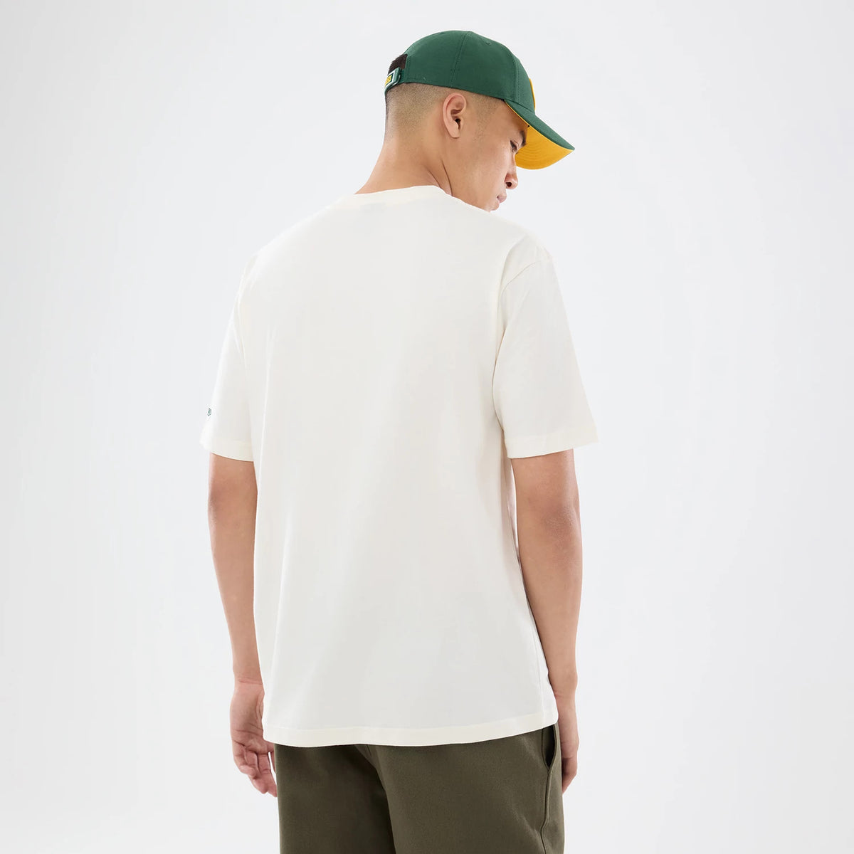 New Era Green Bay Packers NFL Sport Classic Cream T-Shirt, back view on a model wearing a green and yellow cap, showing plain cream fabric with relaxed short sleeves, and a small embroidered New Era logo on the left sleeve.