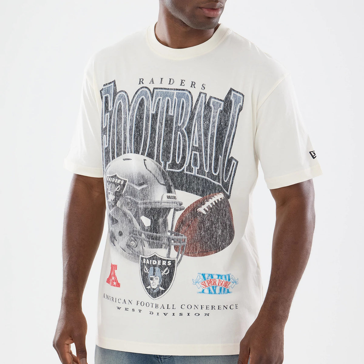 New Era Las Vegas Raiders NFL Sport Classic Cream T-Shirt, front view on-model showcasing a large graphic of a Raiders helmet with a football and FOOTBALL lettering, small patches below, and an embroidered New Era logo on the left sleeve.