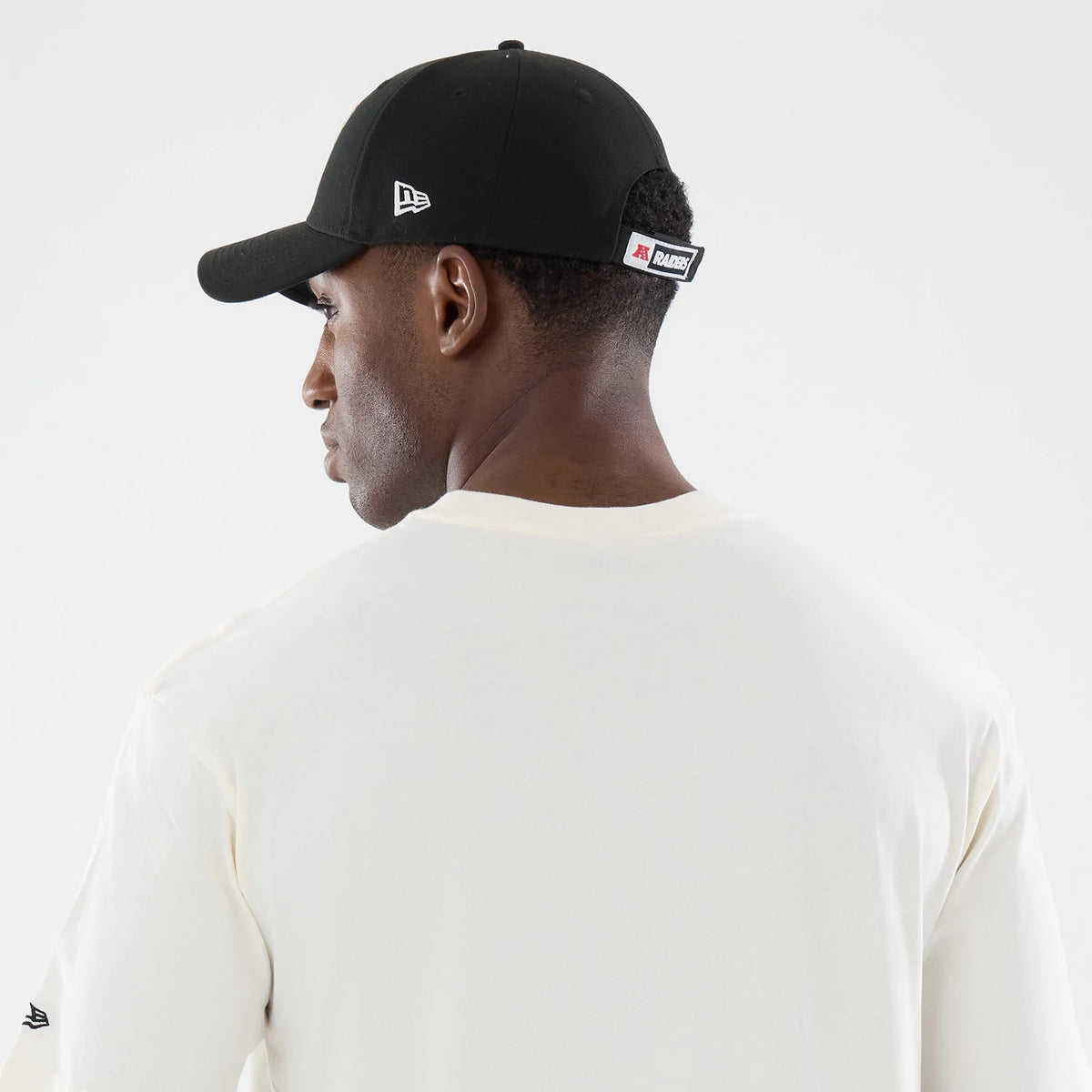 New Era Las Vegas Raiders NFL Sport Classic Cream T-Shirt, back view on a model wearing a black cap, featuring a cream backdrop, small New Era embroidered logo on the sleeve, and a minimalist design with clean lines and no graphics.