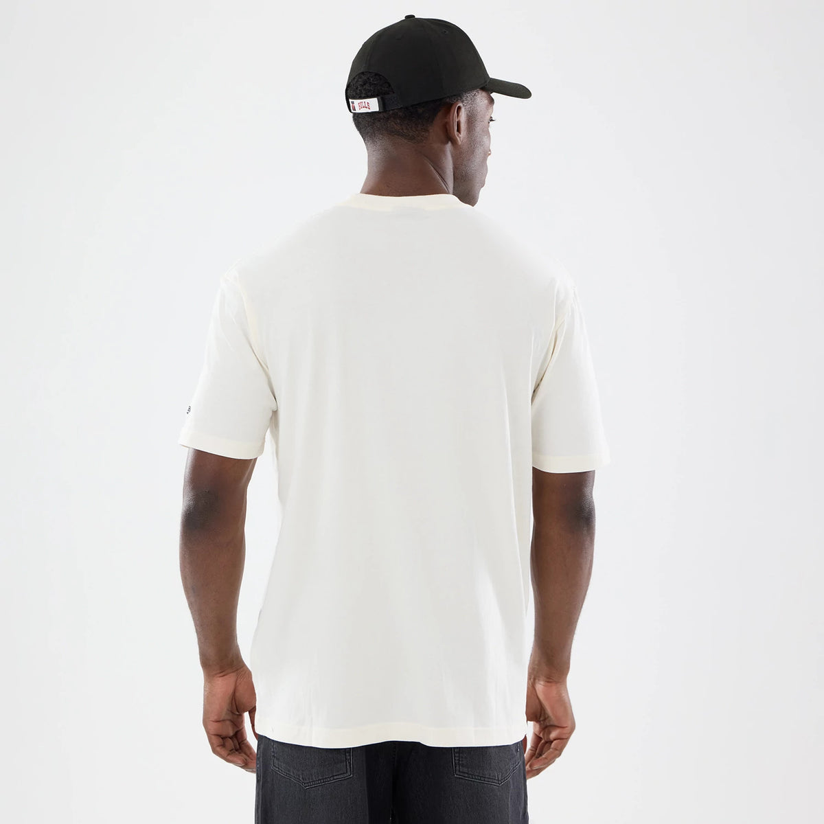 New Era Chicago Bulls NBA Sport Classic Cream T-Shirt, back view on a model wearing a black cap, showing a plain cream design extending across the back and sleeves, with embroidered near the sleeve edge.