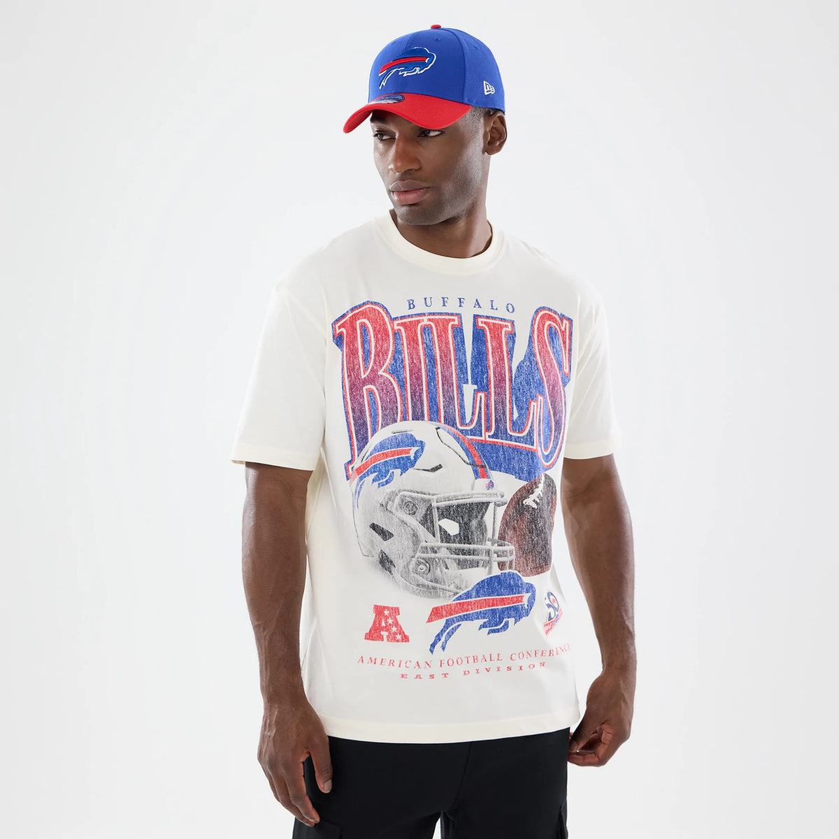 New Era Buffalo Bills NFL Sport Classic Cream T-Shirt, front view on-model featuring large vintage-style Bills lettering and a detailed football helmet graphic, with matching red and blue accents, styled with a New Era red and blue cap.