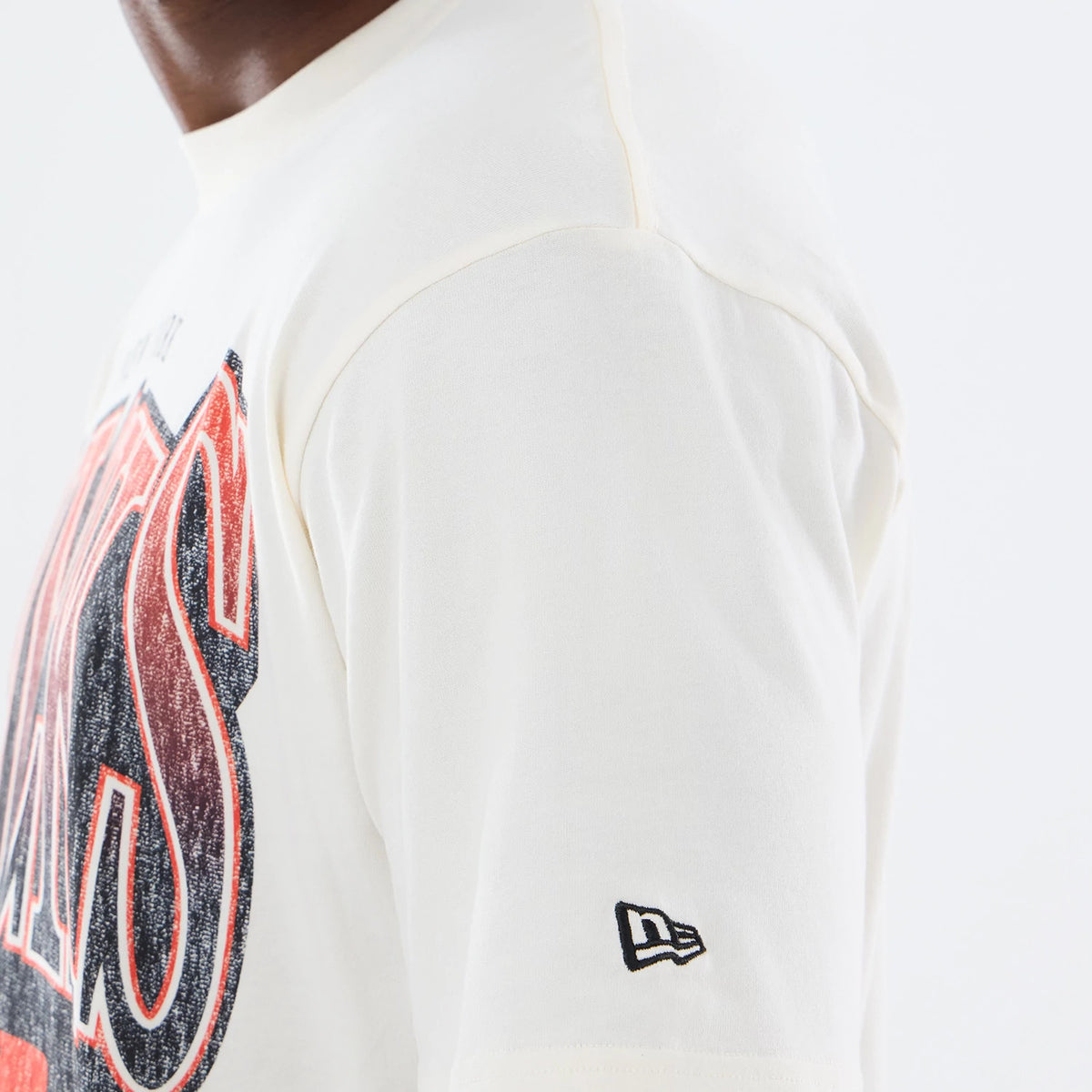 New Era New York Knicks NBA Sport Classic Cream T-Shirt, side view showing the large Knicks graphic detail across the chest in red and black, and an embroidered New Era logo on the sleeve, worn by a model for casual styling.