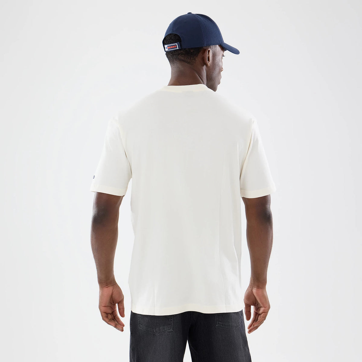 New Era Chicago Bears NFL Sport Classic Cream T-Shirt, back view on a model wearing a navy cap, showing the plain cream fabric with short sleeves, a small embroidered logo on the left sleeve, and a straight hemline.