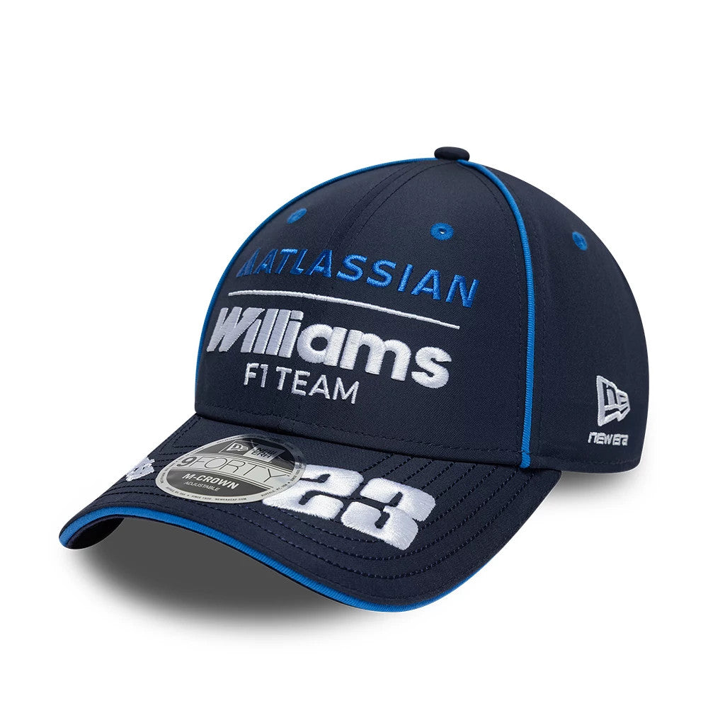 Williams Alex Albon Navy New Era 9FORTY M-Crown Adjustable Cap, three-quarter view showing white and blue embroidered logos on the front panel, a contrasting blue piped trim, and a 9FORTY size sticker on the dark navy curved visor.
