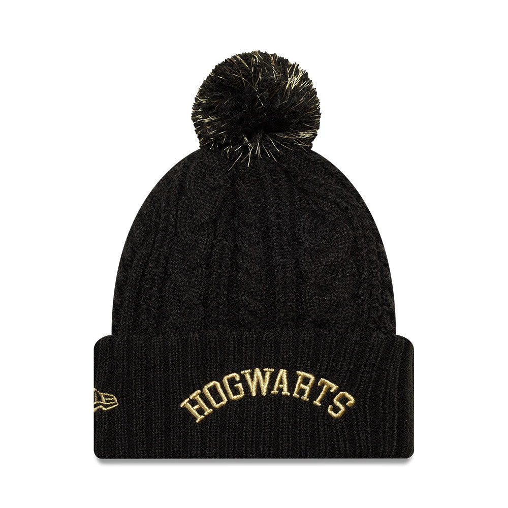 New Era Youth Harry Potter Hogwarts Black Cuff Knit Beanie Hat, front view showcasing the gold embroidered Hogwarts lettering on the cuff, a textured knit pattern on the crown, and a black pom-pom with gold highlights on top.