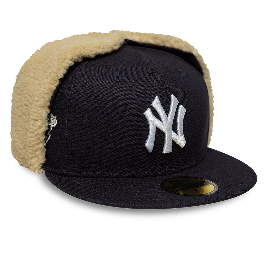 New York Yankees MLB World Series Navy Dogear New Era 59FIFTY Fitted Cap, three-quarter view showing the white raised embroidered NY logo on the front panel, gold 59FIFTY size sticker on the flat navy visor and tan sherpa dogear flaps.