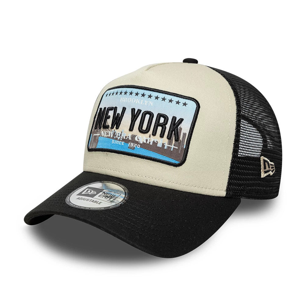 New Era Licence Plate Black 9FORTY A-Frame Trucker Adjustable Cap, three-quarter view showing a large embroidered New York front patch with a skyline graphic, a black curved visor with a 9FORTY size sticker.