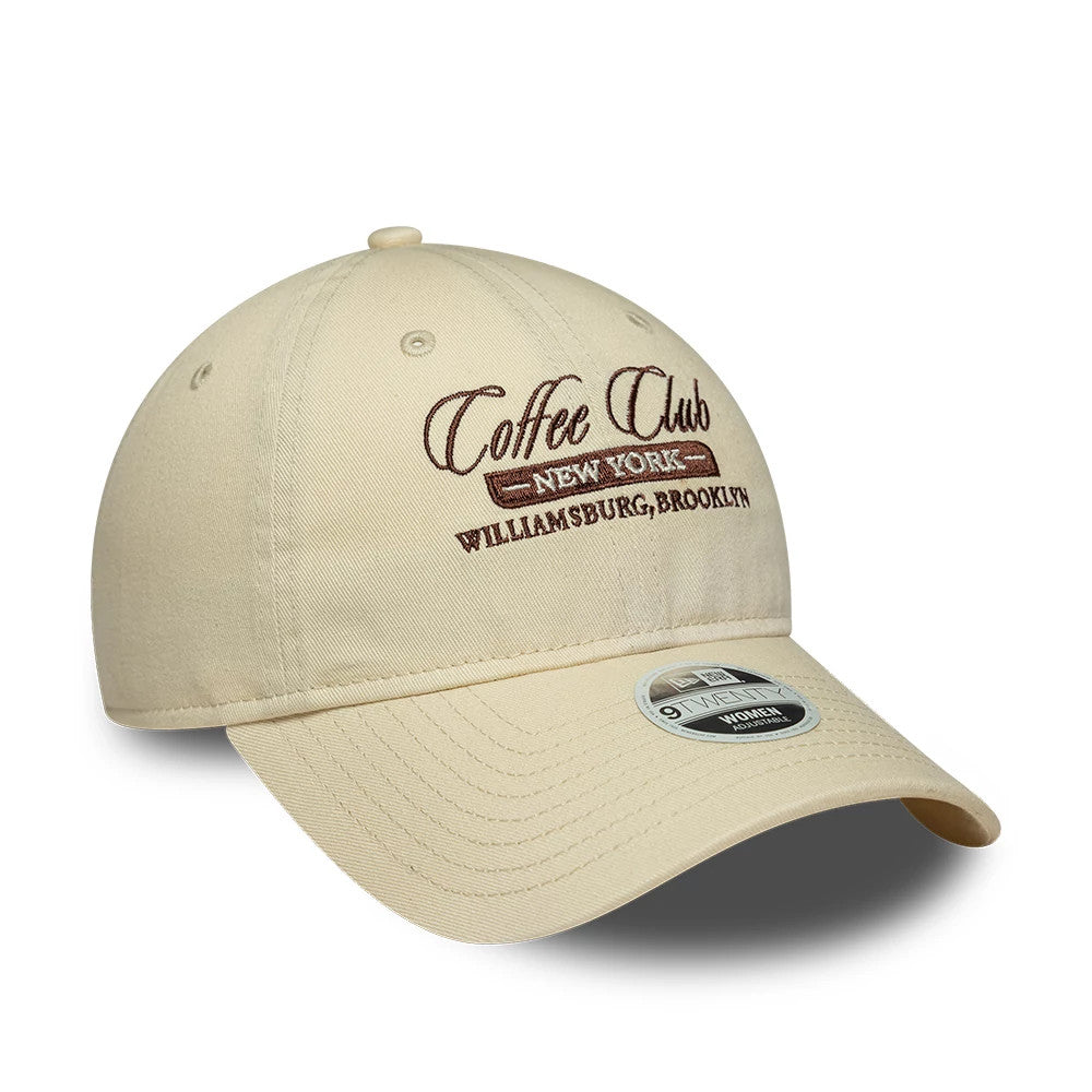 Womens New Era Café Slogan Cream 9TWENTY Adjustable Cap, three-quarter view showing brown Coffee Club embroidery on the front panel, cream curved visor with a 9TWENTY size sticker, and cream eyelets on the unstructured crown.