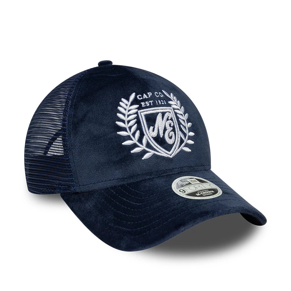 Womens New Era Velour Navy 9FORTY M-Crown A-Frame Trucker Adjustable Cap, three-quarter view showing the white embroidered laurel crest logo on the velour navy front panel, with black mesh side panels and a 9FORTY size sticker on the curved visor.