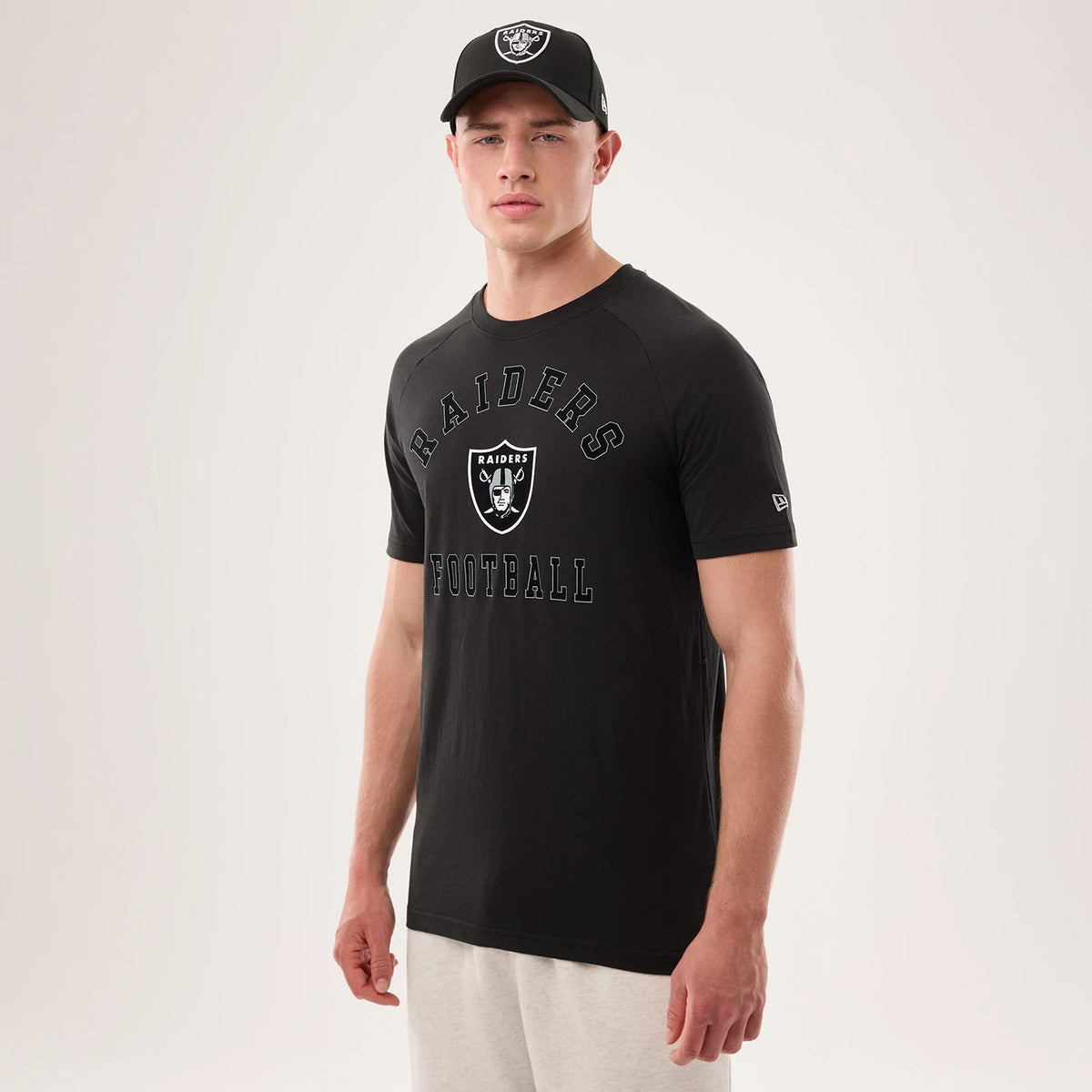 New Era Las Vegas Raiders NFL Sideline 2026 Black T-Shirt, front view on-model displaying the Raiders logo centred on the chest with 'Raiders Football' text above and below, and an embroidered New Era logo on the left sleeve, paired with a black cap.