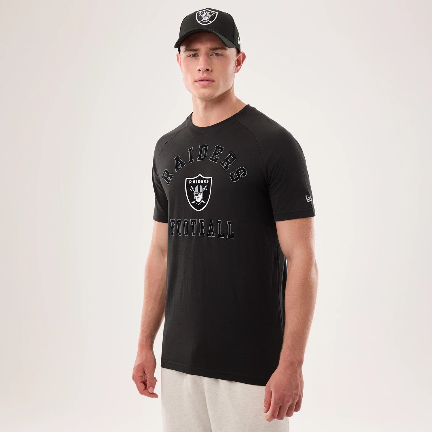New Era Las Vegas Raiders NFL Sideline 2026 Black T-Shirt, front view on-model displaying the Raiders logo centred on the chest with 'Raiders Football' text above and below, and an embroidered New Era logo on the left sleeve, paired with a black cap.