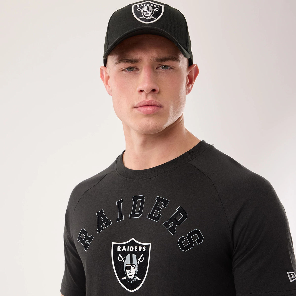 New Era Las Vegas Raiders NFL Sideline 2026 Black T-Shirt, front view on a model wearing a matching cap, featuring Raiders lettering across the chest, an embroidered Raider logo below the text, and a printed New Era logo on the left sleeve.