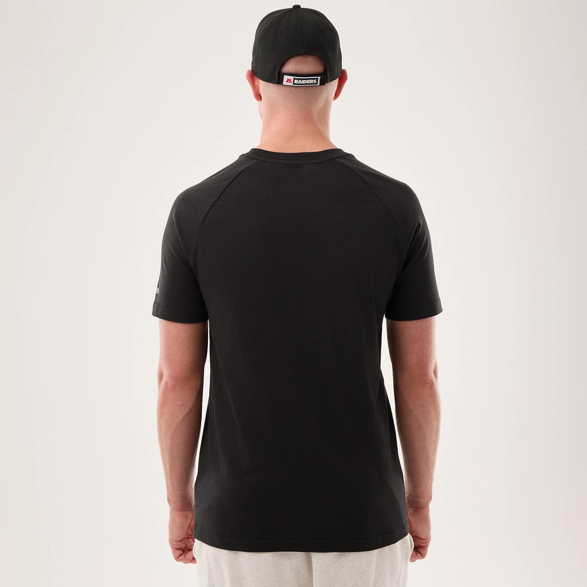 New Era Las Vegas Raiders NFL Sideline 2026 Black T-Shirt, back view on a model with matching black cap, featuring plain black fabric with stitching across the shoulders and a small embroidered New Era logo on the left sleeve.