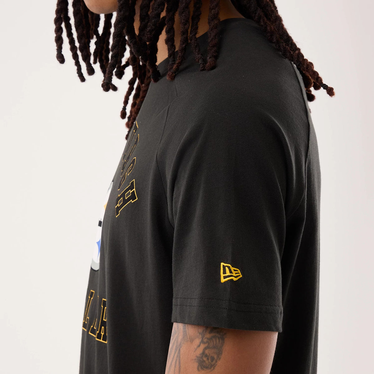 New Era Pittsburgh Steelers NFL Sideline 2026 Black T-Shirt, side view on-model highlighting the yellow embroidered New Era logo on the sleeve, large Pittsburgh Steelers graphics on the front, and a round neckline with stitching detail.
