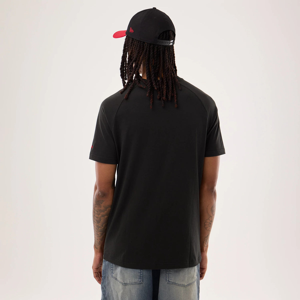 New Era San Francisco 49ers NFL Sideline 2026 Black T-Shirt, back view on a model showing the plain black back of the T-shirt with slightly raglan-style short sleeves, complemented by the model's casual styling with relaxed-fit denim shorts.