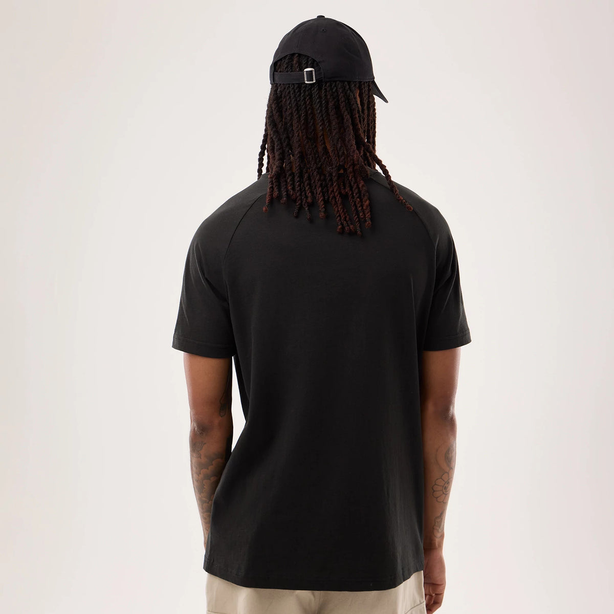 New Era Denver Broncos NFL Sideline 2026 Black T-Shirt, back view on model with cap, displaying a solid black design with raglan sleeves outlined by seams, against beige trousers, highlighting minimalistic style.