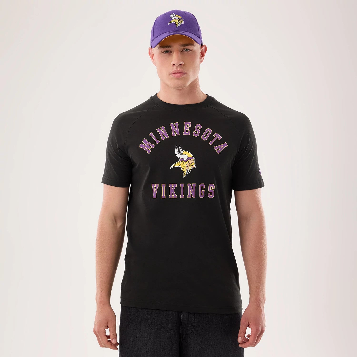 New Era Minnesota Vikings NFL Sideline 2026 Black T-Shirt, front view on a model showing the purple and yellow Minnesota Vikings logo and lettering prominently across the chest, styled with dark jeans.