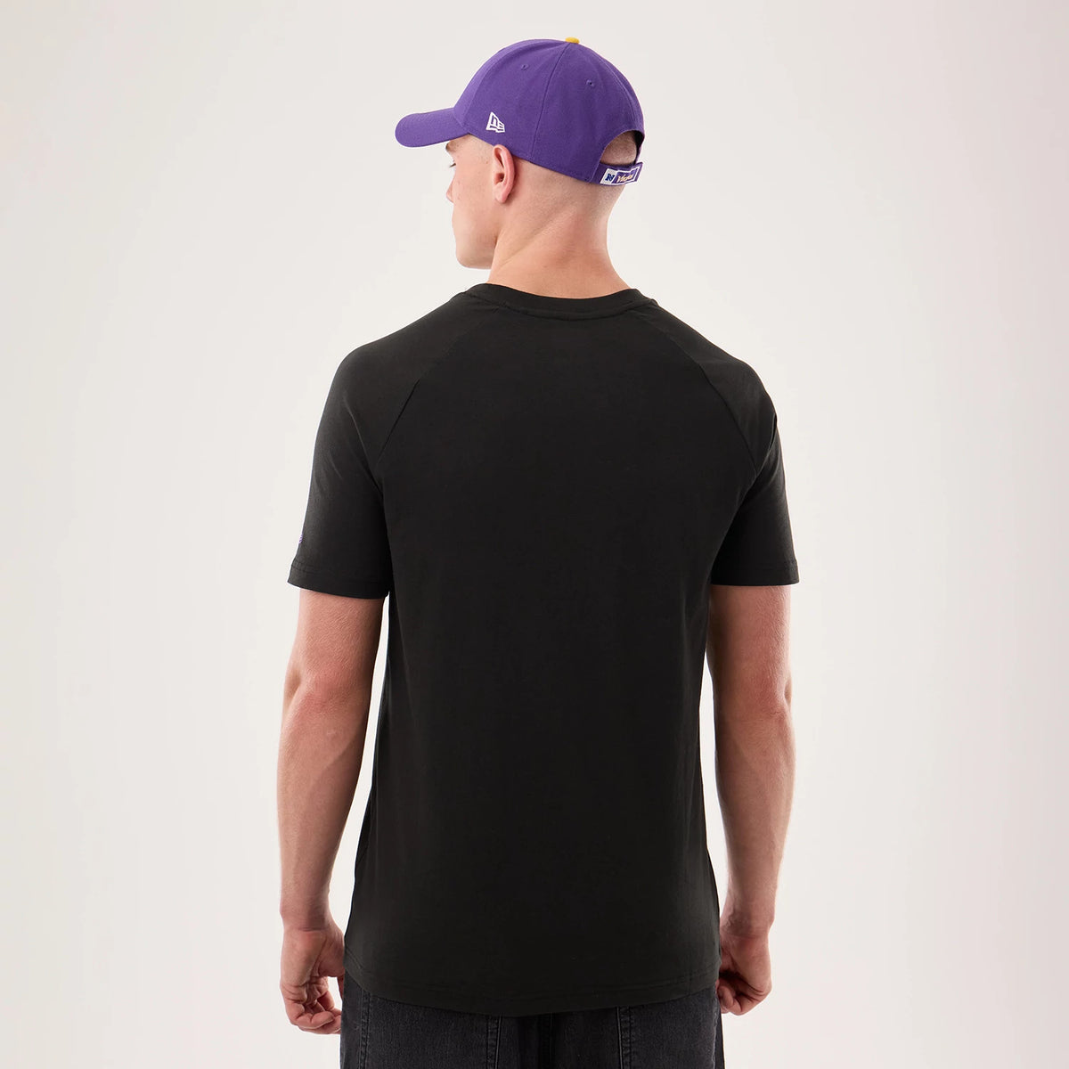 New Era Minnesota Vikings NFL Sideline 2026 Black T-Shirt, back view on-model showing a plain black design with short sleeves and no graphics, styled with a purple cap featuring a white embroidered New Era logo on the side of the crown.