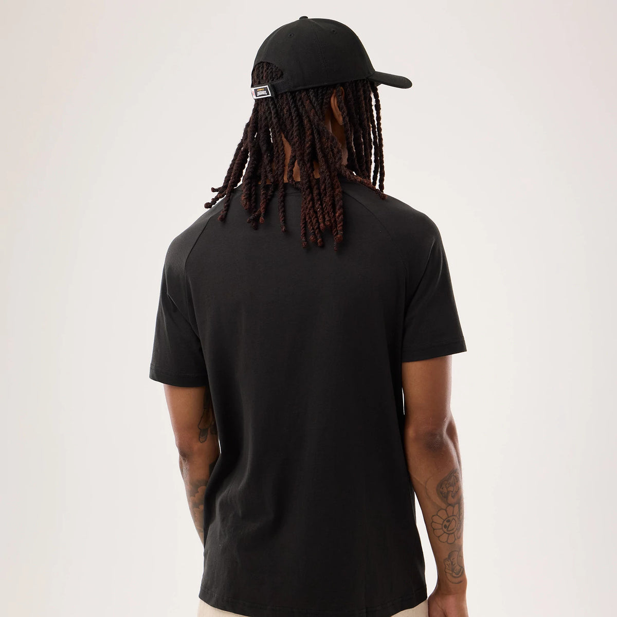 New Era Jacksonville Jaguars NFL Sideline 2026 Black T-Shirt, back view on a model with a black cap, showing the plain black back of the t-shirt with short sleeves and the cap featuring an embroidered logo above the adjustable strap.