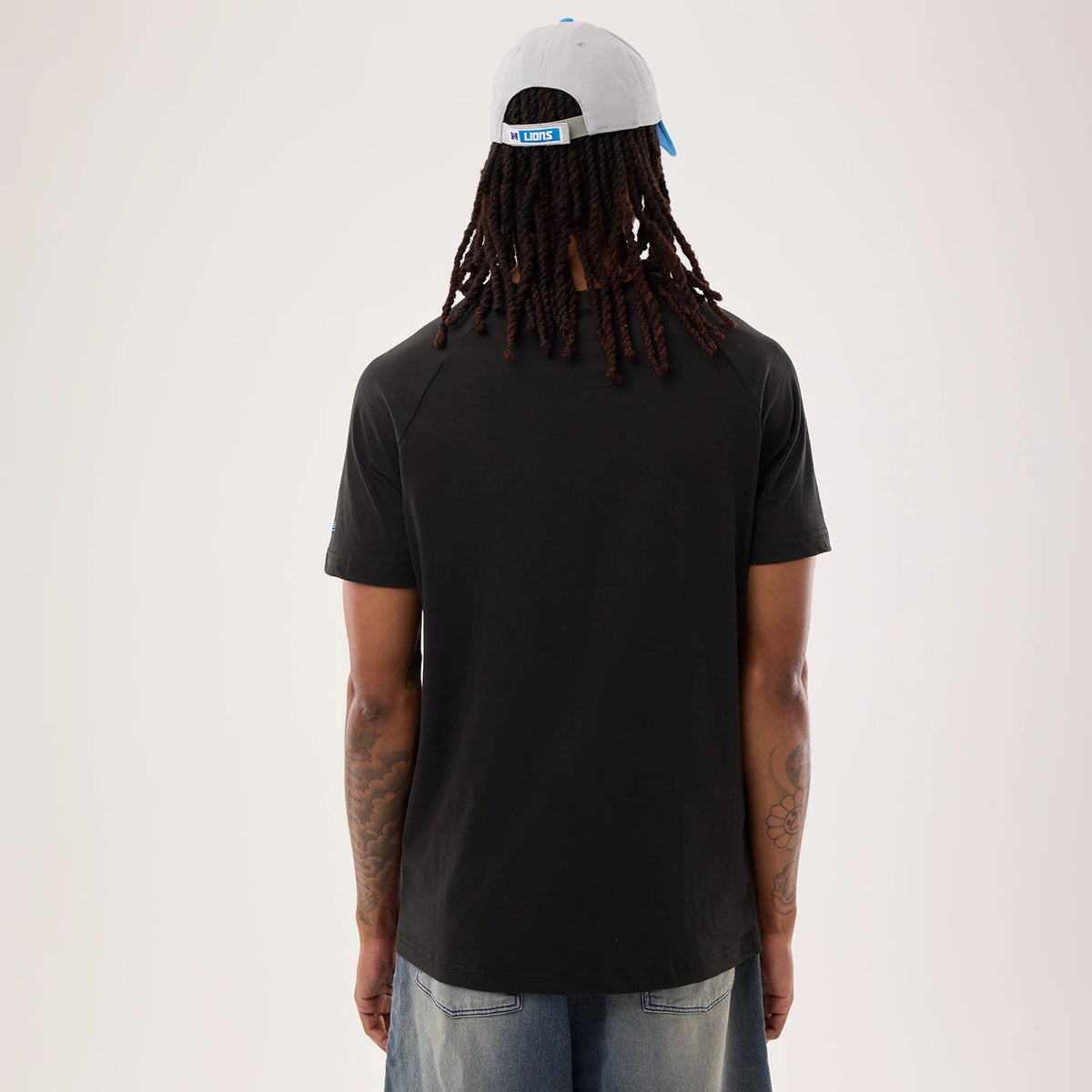 New Era Detroit Lions NFL Sideline 2026 Black T-Shirt, back view on a model paired with light blue jeans and a grey cap, showcasing a plain black back with stitching along the shoulders and sleeves, emphasising the casual look.