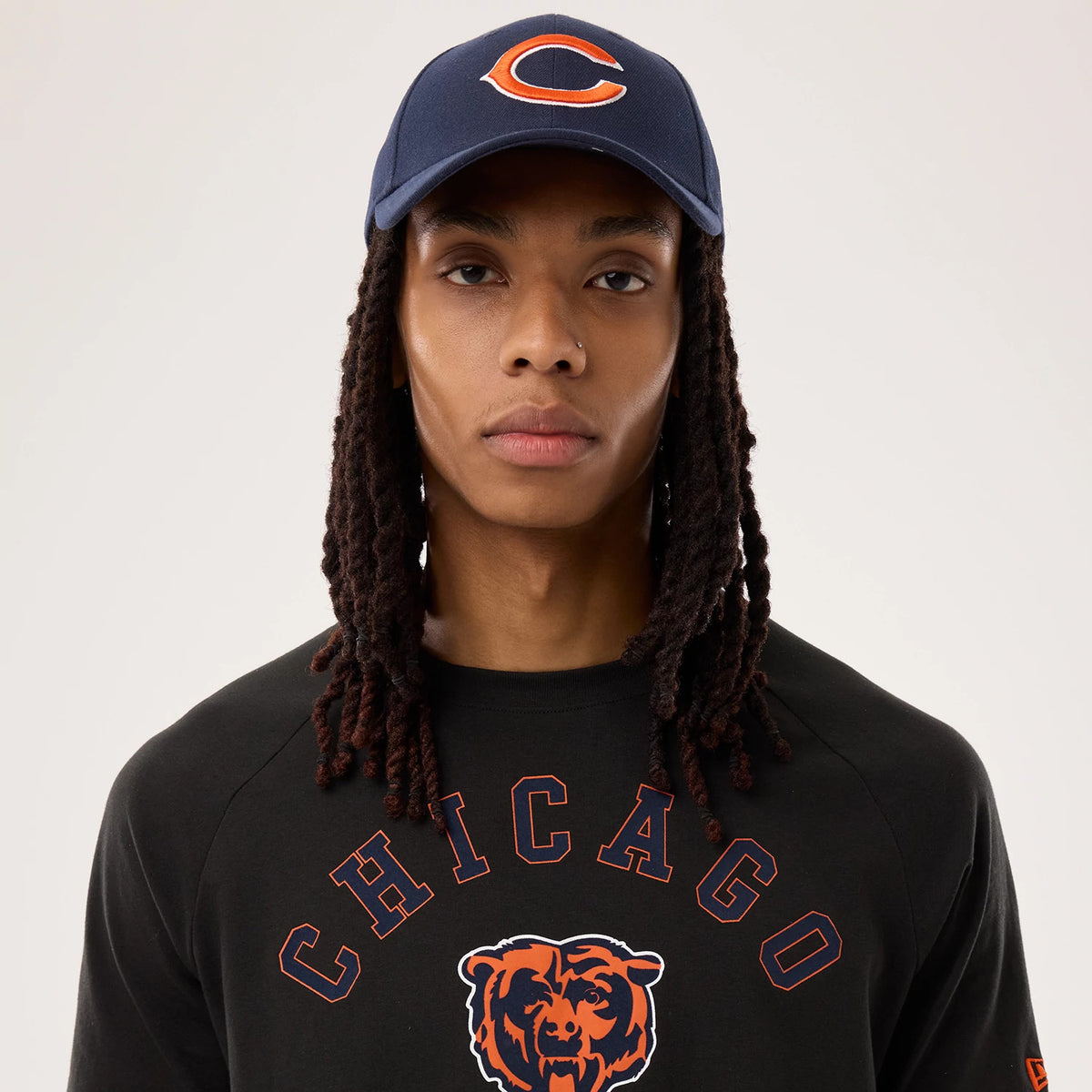 New Era Chicago Bears NFL Sideline 2026 Black T-Shirt, front view on a model paired with a navy cap, featuring 'CHICAGO' in orange lettering above a printed bear graphic on the chest and an orange New Era logo on the left sleeve.