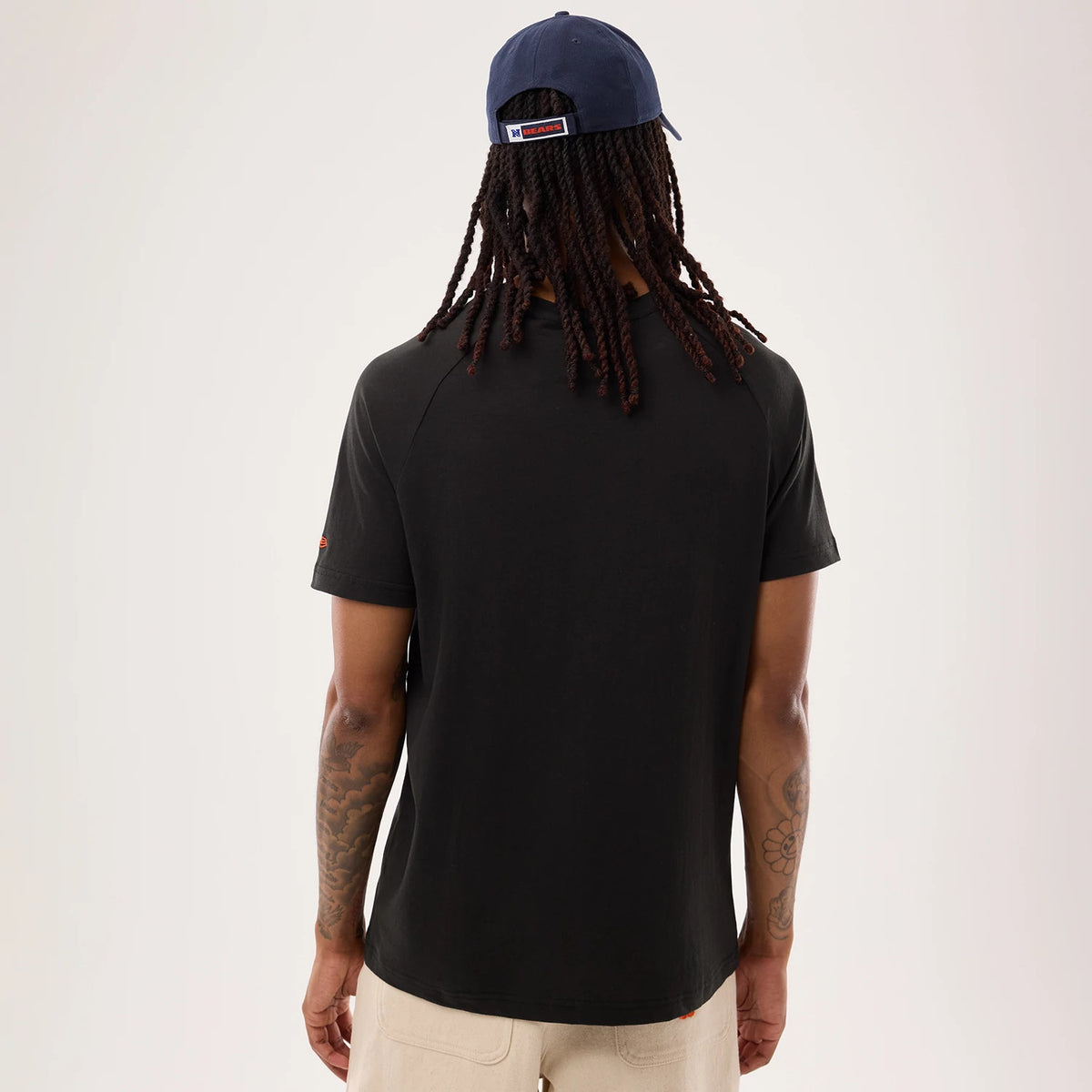 New Era Chicago Bears NFL Sideline 2026 Black T-Shirt, back view on-model showing the plain black back, short sleeves, small embroidered team logo on the left sleeve, and paired with a navy cap featuring a logo tag above the strap.