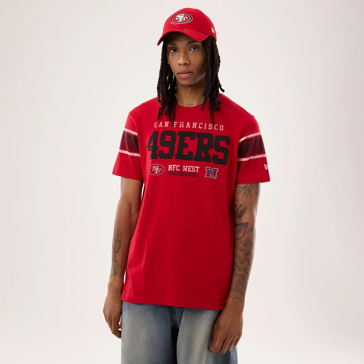 New Era San Francisco 49ers NFL Sideline 2026 Red T-Shirt, front view on a model also wearing a red cap, showing large printed 49ERS logo across the chest, SAN FRANCISCO lettering above, and NFC WEST graphics with stripes on each sleeve.