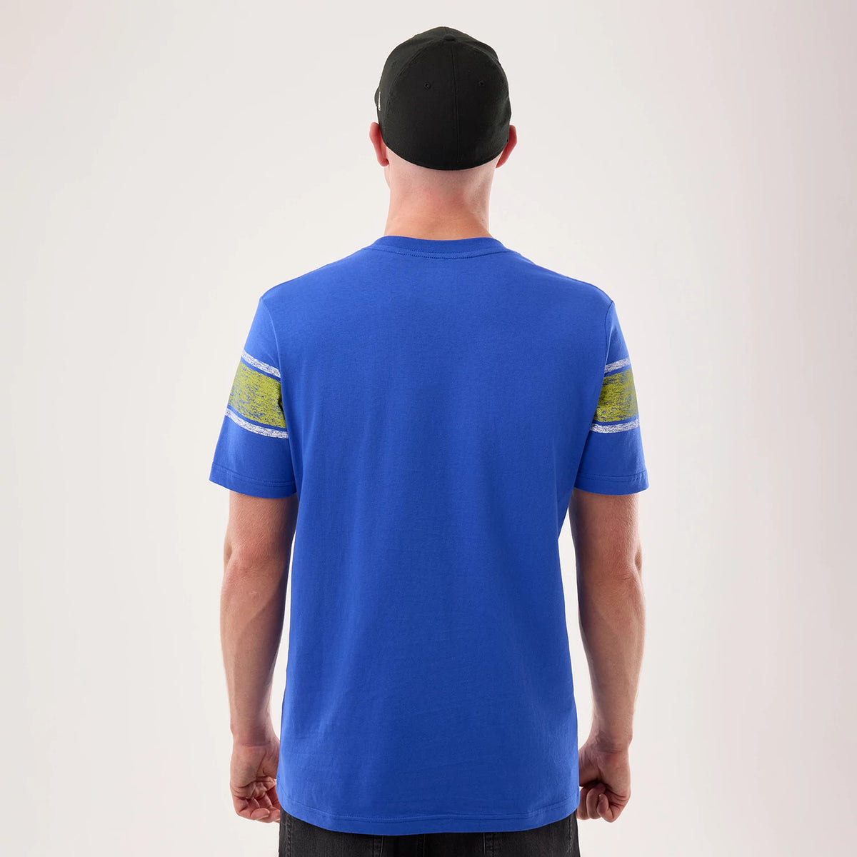 New Era LA Rams NFL Sideline 2026 Bright Blue T-Shirt, back view on-model showing the rich blue colour with sleeve graphics in yellow and white, a clean round neckline, and a simple silhouette matched with a dark cap for a casual look.