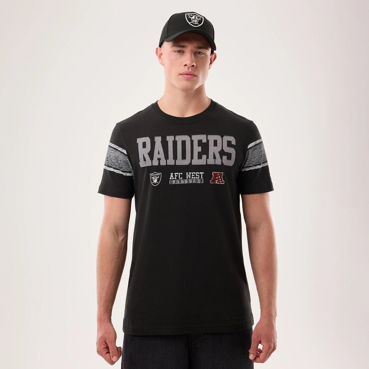 New Era Las Vegas Raiders NFL Sideline 2026 Black T-Shirt, front view on a model displaying grey Raiders lettering across the chest, an embroidered team logo below, and textured stripes on the sleeves with the model wearing a matching black cap.