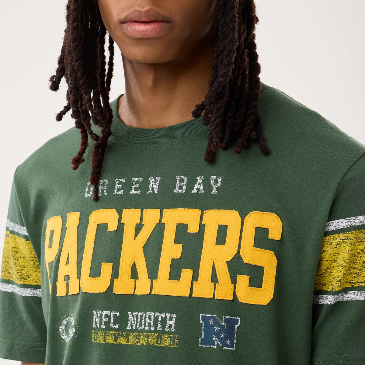 New Era Green Bay Packers NFL Sideline 2026 Dark Green T-Shirt, front view on-model highlighting the yellow PACKERS lettering across the chest, weathered green and yellow stripes on the sleeves, and smaller embroidered N and team logo patches.