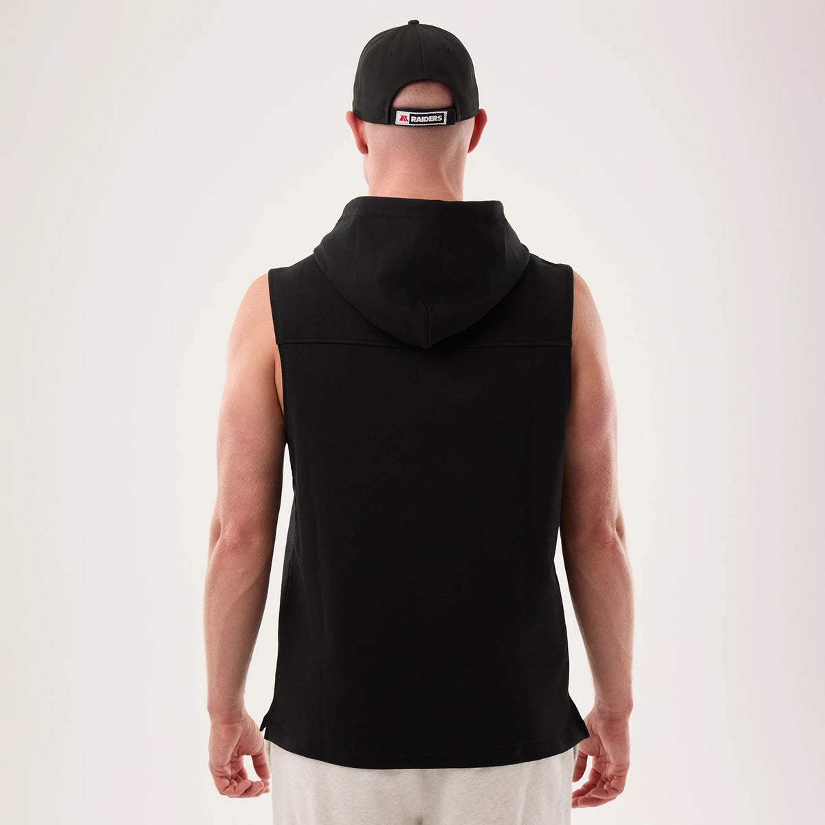 New Era Las Vegas Raiders NFL Sideline 2026 Black Tank Top, back view on a model showing the sleeveless design and attached black hood, paired with a matching black cap featuring a Raiders logo on the centre back strap.