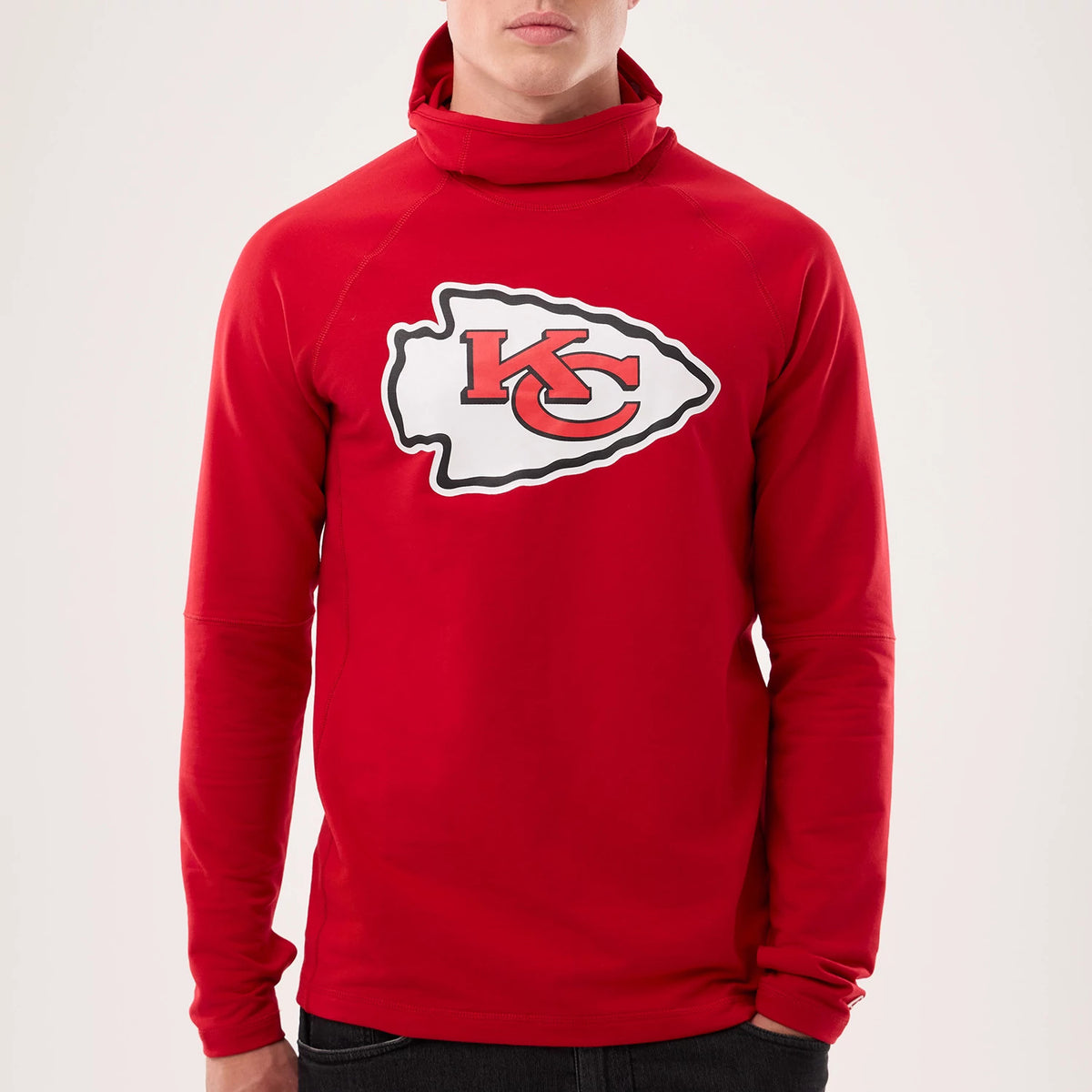 New Era Kansas City Chiefs NFL Sideline 2026 Red Balaclava Hoodie, front view on a model showing the Chiefs logo prominently on the chest, a high snug collar extending from the neck, and long fitted sleeves against the bright red fabric.