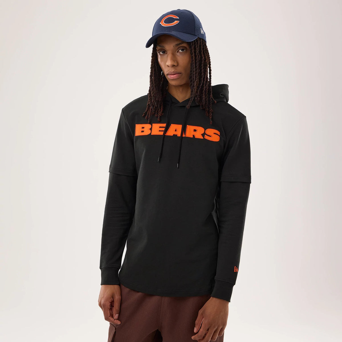 New Era Chicago Bears NFL Sideline 2026 Black Double Sleeve Hoodie, front view on a model also wearing a Bears cap, featuring the orange BEARS lettering across the chest and a small embroidered New Era logo on the left sleeve hem.