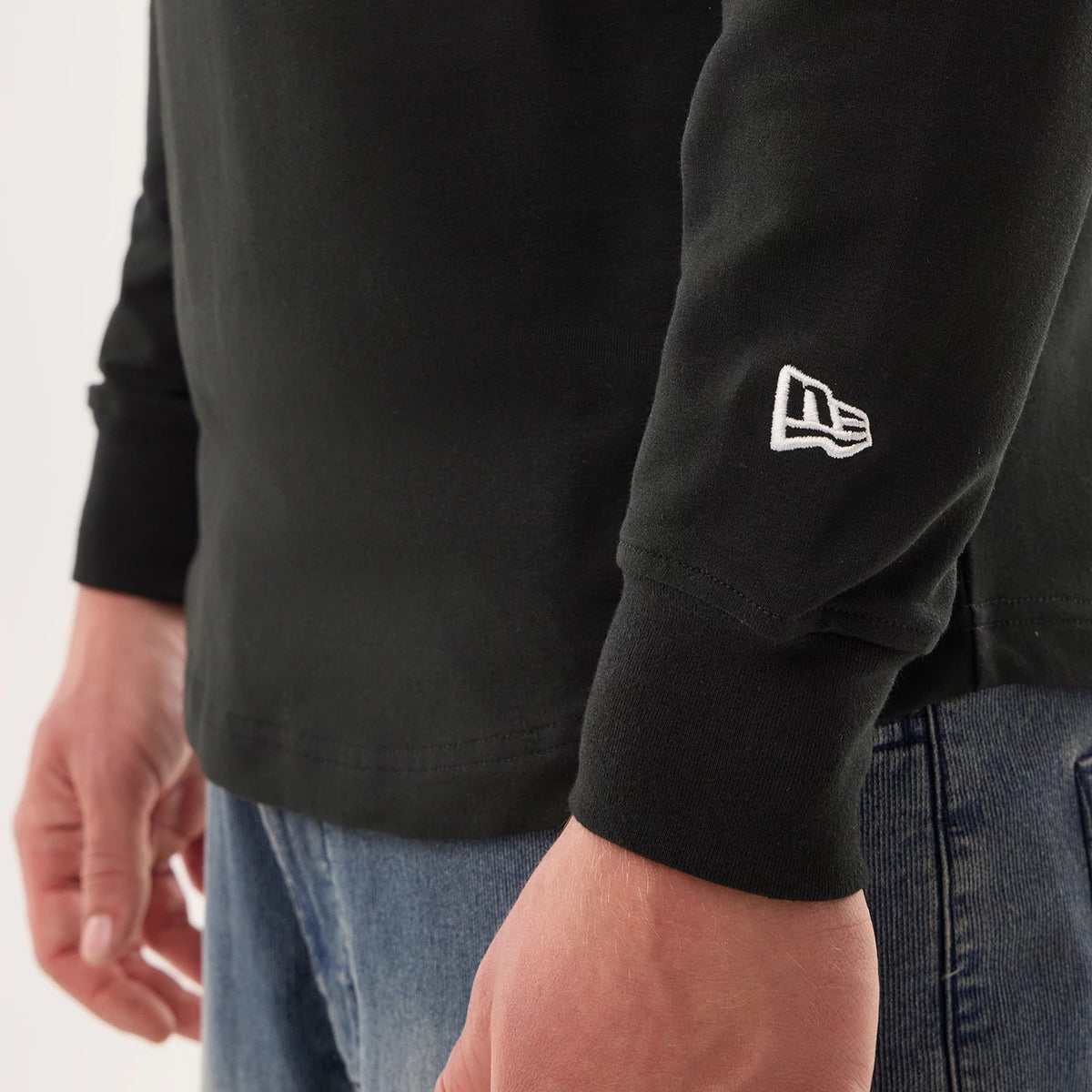 New Era Philadelphia Eagles NFL Sideline 2026 Black Double Sleeve Hoodie, side view showcasing the black sleeve with an embroidered white New Era logo near the cuff, worn by a model styled with blue denim jeans.