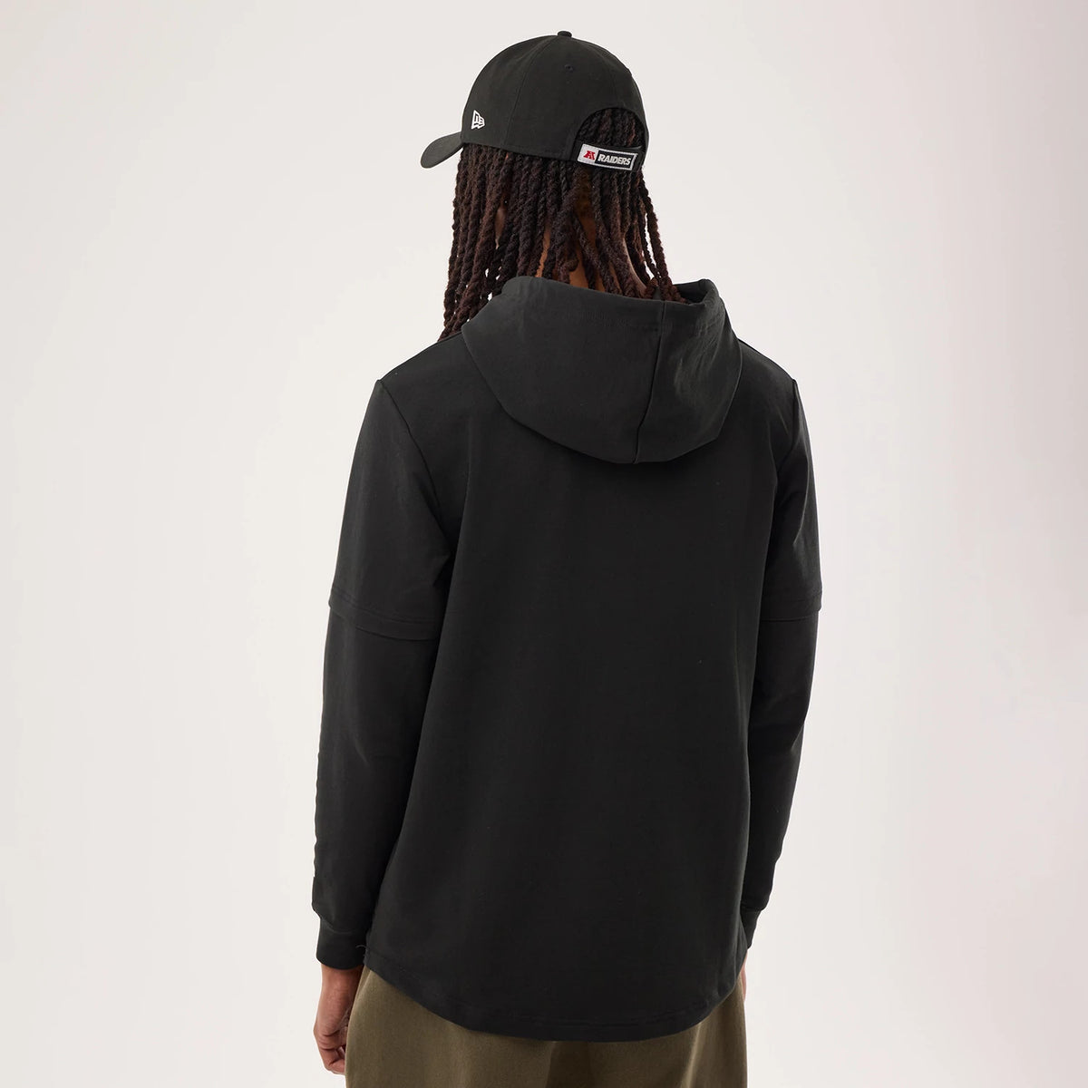 New Era Las Vegas Raiders NFL Sideline 2026 Black Double Sleeve Hoodie, back view on a model showing the solid black design with a hood, double sleeve details, and seam lines, paired with a black cap featuring an embroidered New Era logo on the side.