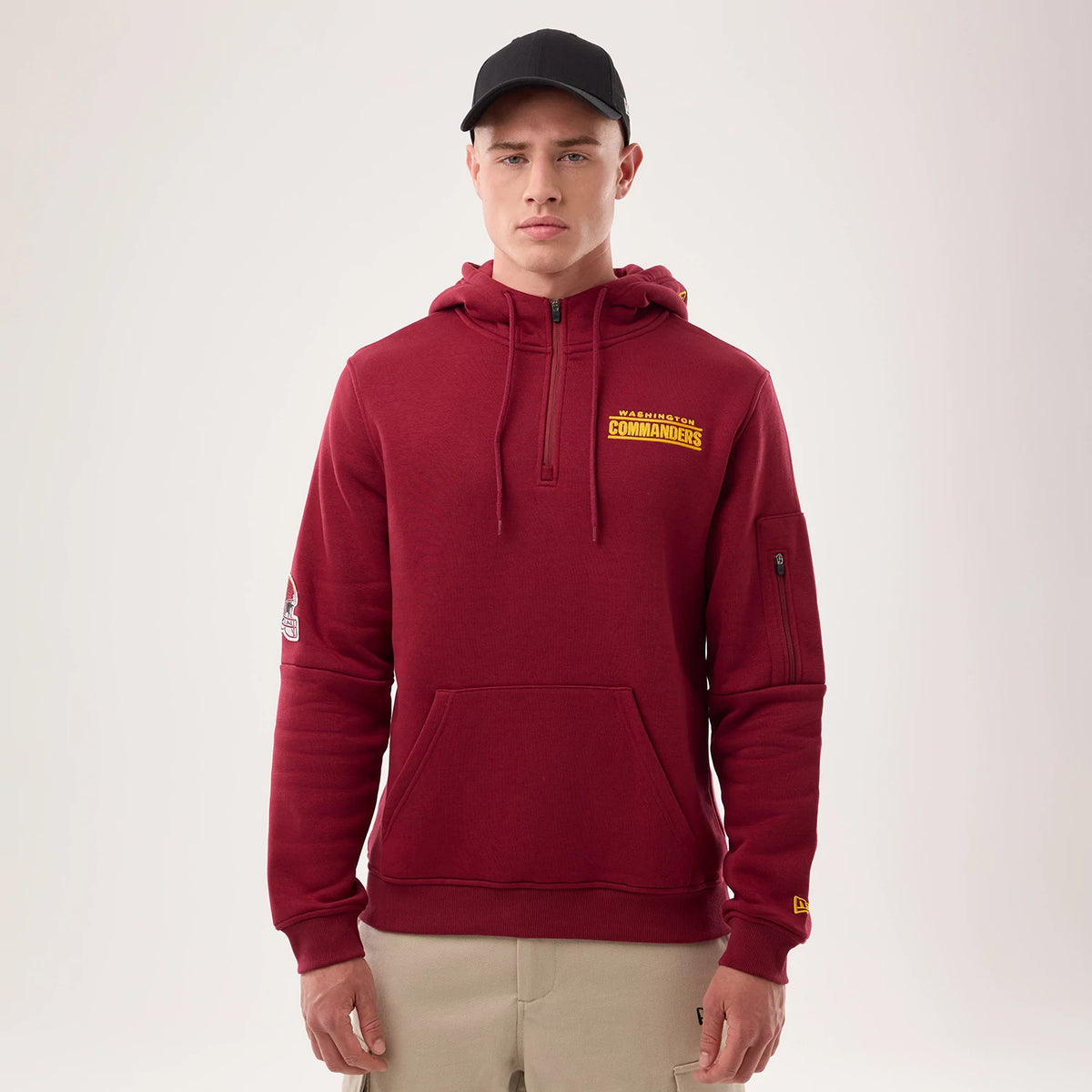 New Era Washington Commanders NFL Sideline 2026 Dark Red Pullover Hoodie, front view on-model showcasing a yellow embroidered Washington Commanders logo on the chest, a zippered sleeve pocket, and New Era logo on the left cuff.