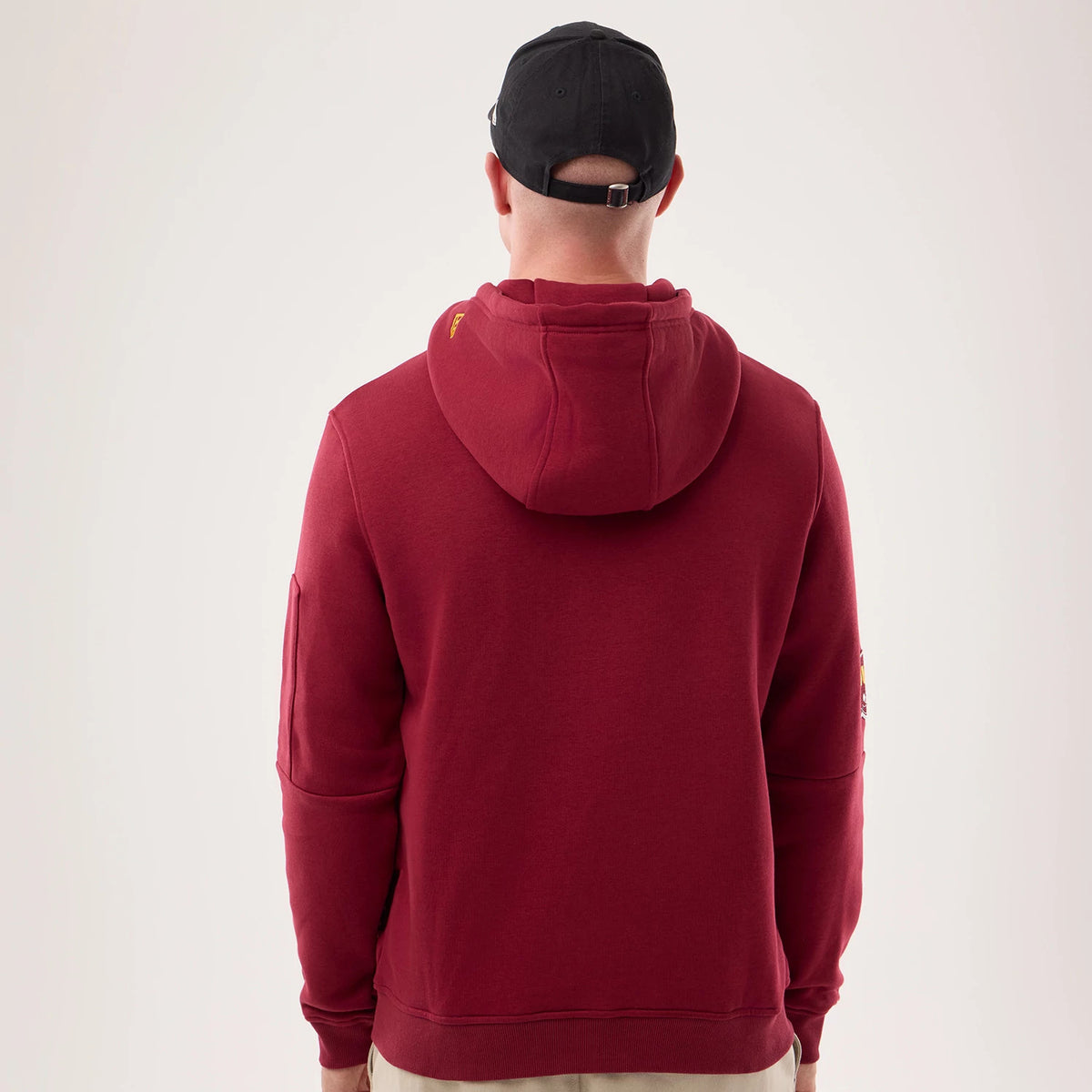 New Era Washington Commanders NFL Sideline 2026 Dark Red Pullover Hoodie, back view on model with matching hood, showing a dark red design with a pouch pocket on the sleeve and team logo details near the shoulder seams.