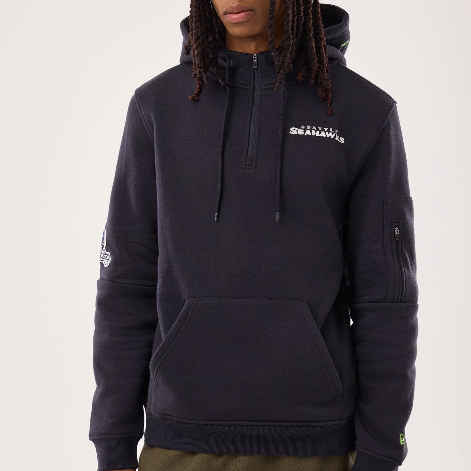 New Era Seattle Seahawks NFL Sideline 2026 Navy Pullover Hoodie, front view on a model showing the front pouch pocket and a half-zip collar, with the embroidered Seattle Seahawks logo on the left chest and an embroidered patch on the left sleeve.