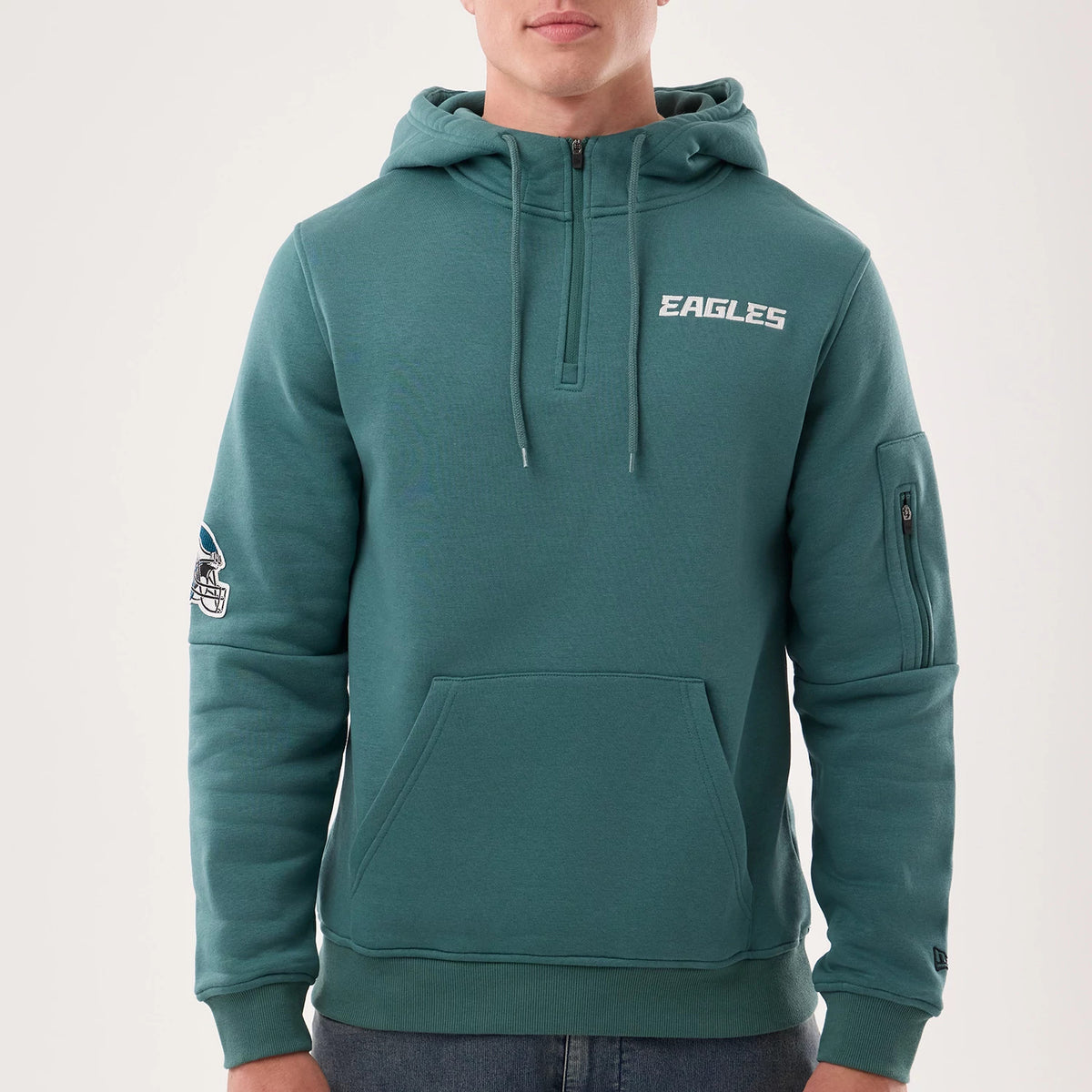 New Era Philadelphia Eagles NFL Sideline 2026 Dark Green Pullover Hoodie, front view on-model showing white embroidered Eagles text on the chest, a kangaroo pocket, a team logo patch on the left sleeve, and a zippered pocket on the right arm.