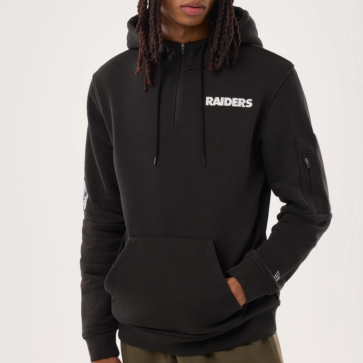 New Era Las Vegas Raiders NFL Sideline 2026 Black Pullover Hoodie, front view on-model featuring the white embroidered RAIDERS text on the chest, a zipper at the neck, zip pocket on the sleeve, and New Era flag logo on the left cuff.